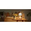 A candle warmer lamp sits on a side table next to a couch, with a vase of yellow tulips and a decorative vase. Náhled obrázku produktu