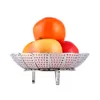 A stainless steel steamer basket filled with fruit, including an orange, apples, and a red fruit, against a white background. Produktbild-Vorschau
