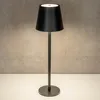 A black LED table lamp with a fabric shade is placed on a white surface against a textured gray wall. Produktbild-Vorschau