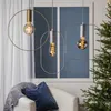 Three modern pendant lights with spiral filament bulbs hang above a chair with a blanket and pillow. A Christmas tree with lights is visible on the right. Podgląd zdjęcia produktu