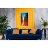 A living room scene with a blue sofa, decorative pillows, and a large framed picture of Manhattan on a yellow wall. Produktbild-Vorschau