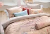 A close-up view of a bed with multiple pillows and a duvet cover featuring a floral and bird pattern. Produktbild-Vorschau