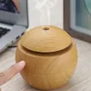 A finger is pressing the button of a wooden sphere-shaped humidifier emitting steam, with a laptop and a framed picture in the background. Produktbild-Vorschau