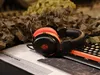 A gaming headset is placed on a surface with camouflage netting in the background. Anteprima dell’immagine prodotto