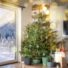 A Christmas tree decorated with ornaments and lights, standing in a room with a window showing a snowy landscape. Podgląd zdjęcia produktu