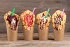 Four bubble waffles filled with ice cream and toppings stand in brown paper cups on a wooden surface. Náhľad obrázku produktu