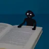 A black bookmark with LED eyes sits on an open book. Voir les images du produit