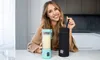 A woman is sitting at a table with a portable blender and a black carrying case. Náhľad obrázku produktu