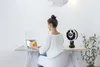 A woman is working on her laptop at a desk with a fan next to her. Produktbild-Vorschau