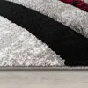 A close-up view of a rug with abstract geometric patterns in shades of gray, black, and red. Produktbild-Vorschau