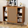 A wooden sideboard with a cane door, filled with books and decorative items, placed in a room with wooden flooring. Produktbild-Vorschau