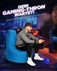A man is playing a video game while sitting on a blue beanbag chair in a dimly lit room with gaming equipment. Produktbild-Vorschau