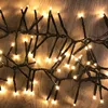 A close-up shot of a string of warm white LED cluster lights on a wooden surface. Produktbild-Vorschau