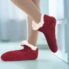 Rote gestrickte Hausschuhe-Socken mit weißem Kunstfellfutter, getragen an den Füßen einer Person, ein Fuß angehoben Náhľad obrázku produktu