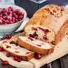 A loaf of cranberry bread, sliced, with a bowl of cranberries in the background. Voir les images du produit