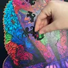 A hand is placing a puzzle piece into a wooden jigsaw puzzle depicting a colorful cat. Náhľad obrázku produktu