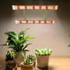 Two LED grow lights are suspended above a collection of potted plants on a wooden surface. Náhľad obrázku produktu