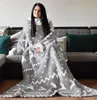 A woman is sitting on a couch, wrapped in a blanket with sleeves. Produktbild-Vorschau