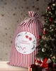A large red and white striped Christmas sack with a Merry Christmas design is placed next to a decorated Christmas tree. Podgląd zdjęcia produktu
