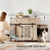 A woman is interacting with a dog crate furniture piece, and a dog is exiting the side door. Náhled obrázku produktu