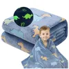 A young boy is wrapped in a blue blanket with dinosaur patterns. The blanket is folded in the background. Náhled obrázku produktu