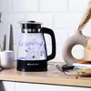 A glass kettle with boiling water is shown on a wooden countertop next to a vase and some cookies. Anteprima dell’immagine prodotto