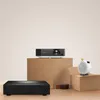 A collection of electronic devices, including a projector and a speaker, arranged on a wooden surface and a cabinet. Náhled obrázku produktu