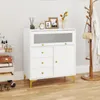 A white cabinet with drawers and a glass door sits on a wooden floor, with a coat rack and a rolling cart nearby. Produktbild-Vorschau