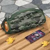 A camouflage portable speaker and a smartphone are placed on a wooden surface, with fallen leaves scattered around. Náhľad obrázku produktu