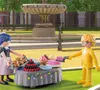 Two Playmobil figures are setting up a picnic with a table full of desserts in a park setting with a fountain in the background. Anteprima dell’immagine prodotto