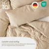A close-up view of folded taupe-colored muslin bedding, featuring a pillow and duvet cover. Text overlays highlight product features and certifications. Produktbild-Vorschau