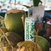 A can of coconut water sits amongst a pile of fresh coconuts. Produktbild-Vorschau