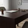 A close-up view of a dark wood desk with a laptop, a potted plant, a mug, and a notebook. Produktbild-Vorschau