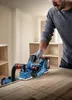 A man is using a Bosch cordless planer on a wooden surface in a workshop or home improvement setting. Podgląd zdjęcia produktu