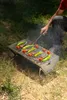 A person is grilling food on a portable grill outdoors on the grass. Produktbild-Vorschau