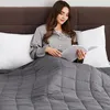 A woman is reading a book in bed, covered by a weighted blanket. Produktbild-Vorschau