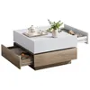 A modern coffee table with a white top and wood-grain base, featuring two open drawers. Produktbild-Vorschau