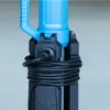 A close-up view of the base of a blue and black work light, showing the power cord wrapped around it. Náhled obrázku produktu