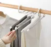 Weißer mehrstöckiger Hosenbügel mit Metallstangen, der graue und weiße Hosen an einer Holzschrankstange hält, eine Hand zieht eine der Stangen heraus Náhľad obrázku produktu