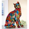 A colorful, artistic cat figurine sits on a white surface with a blurred background. Produktbild-Vorschau