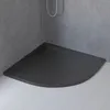 A dark gray, curved shower tray with a drain in the corner, set against gray tiled walls and a white wooden floor. Produktbild-Vorschau