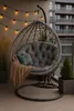 A hanging egg chair with cushions and a blanket on a balcony, decorated with string lights. Voir les images du produit