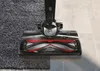 A close-up shot of a vacuum cleaner head transitioning from a carpet to a tiled floor, demonstrating its cleaning capability. Produktbild-Vorschau