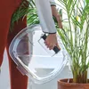 A person is watering a plant using a clear container filled with water. Produktbild-Vorschau