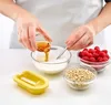 A person is pouring honey into a bowl of milk, with raspberries and oats in separate bowls nearby, and a yellow popsicle mold in the foreground. Produktbild-Vorschau