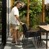 A man is standing next to a stack of outdoor chairs near a table in a garden setting. Produktbild-Vorschau