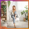 A woman is sitting in a hanging chair in a room with plants and shelves. Náhled obrázku produktu
