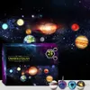 A product box with a space-themed design, featuring planets and galaxies, with small spherical ornaments in the foreground. Náhled obrázku produktu