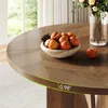 A close-up of a round wooden dining table with a bowl of persimmons and a vase of flowers on it, with a window in the background. Voir les images du produit
