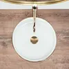 A top-down view of a white ceramic sink with a gold rim and a gold faucet, placed on a wooden surface. Produktbild-Vorschau